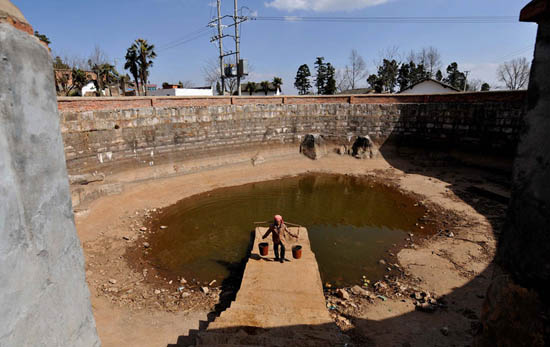 雨古村民小组的一名农妇在接近干涸的蓄水池内挑水用于家里的牲畜饮水